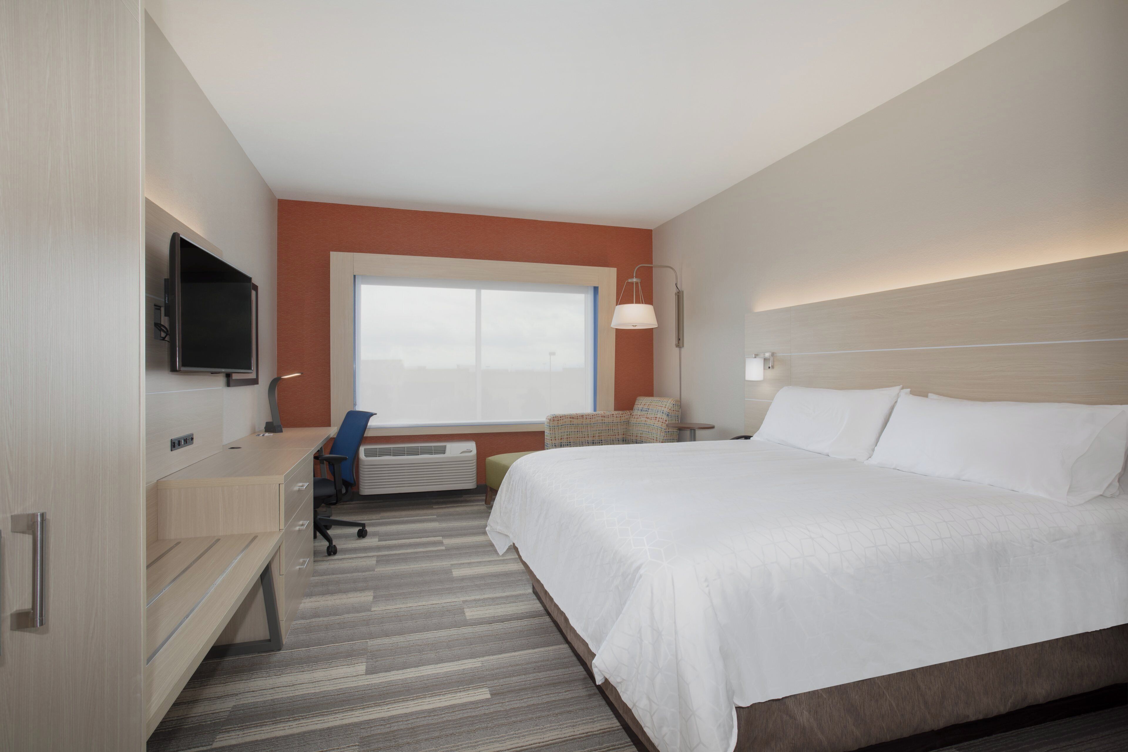 A hotel room with a bed, desk, chair, television, and a window.