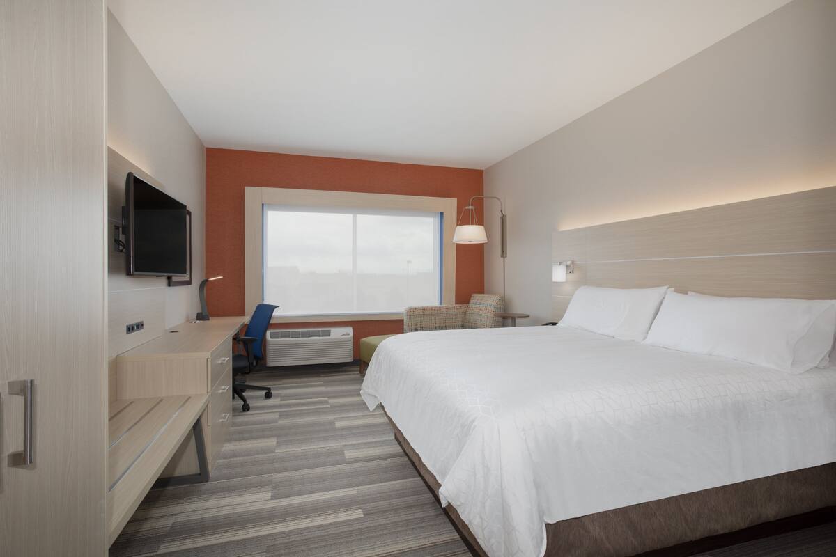 A hotel room with a bed, desk, chair, TV, and window.