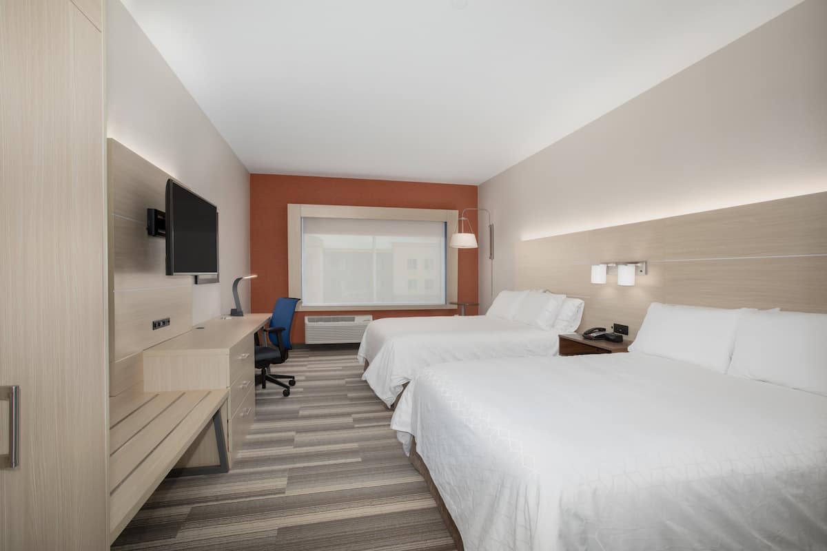 A hotel room with two beds, a desk, a chair, a TV, and a window.