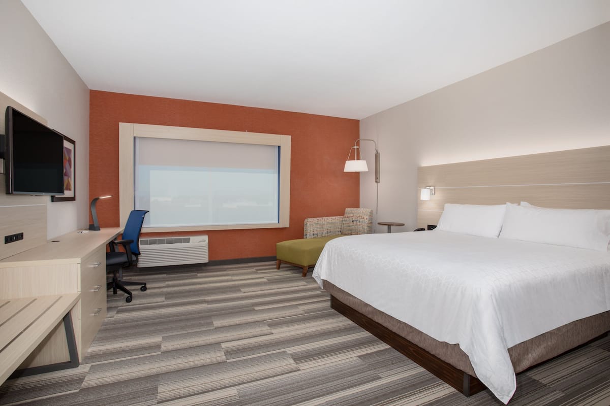 A hotel room with a large bed, a desk with a chair, a television, and a window with blinds.