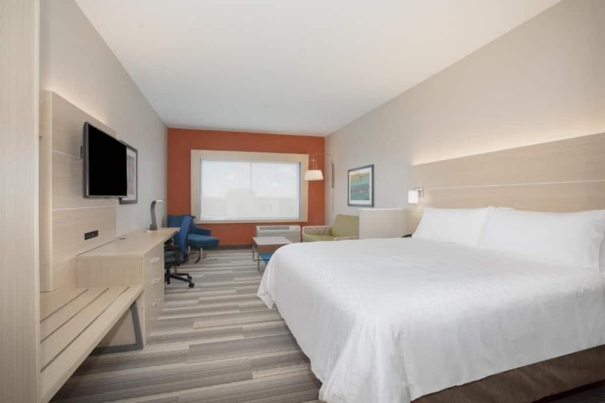 A hotel room with a bed, desk, chair, TV, and a window.