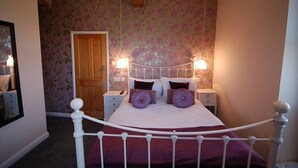 A bedroom with a four-poster bed, floral wallpaper, and bedside lamps. - The Old Red Lion (Thame)