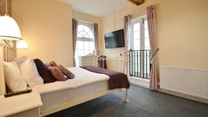 A bedroom with a bed, a TV, a window, and a radiator. - The Old Red Lion (Thame)