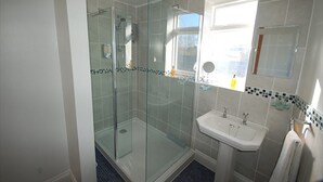 A modern bathroom with a glass-enclosed shower, a sink, and a window. - The Old Red Lion (Thame)