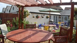 A wooden pergola with a round table and chairs, a hanging flower basket, and a small outdoor seating area with a table and chairs. - The Old Red Lion (Thame)