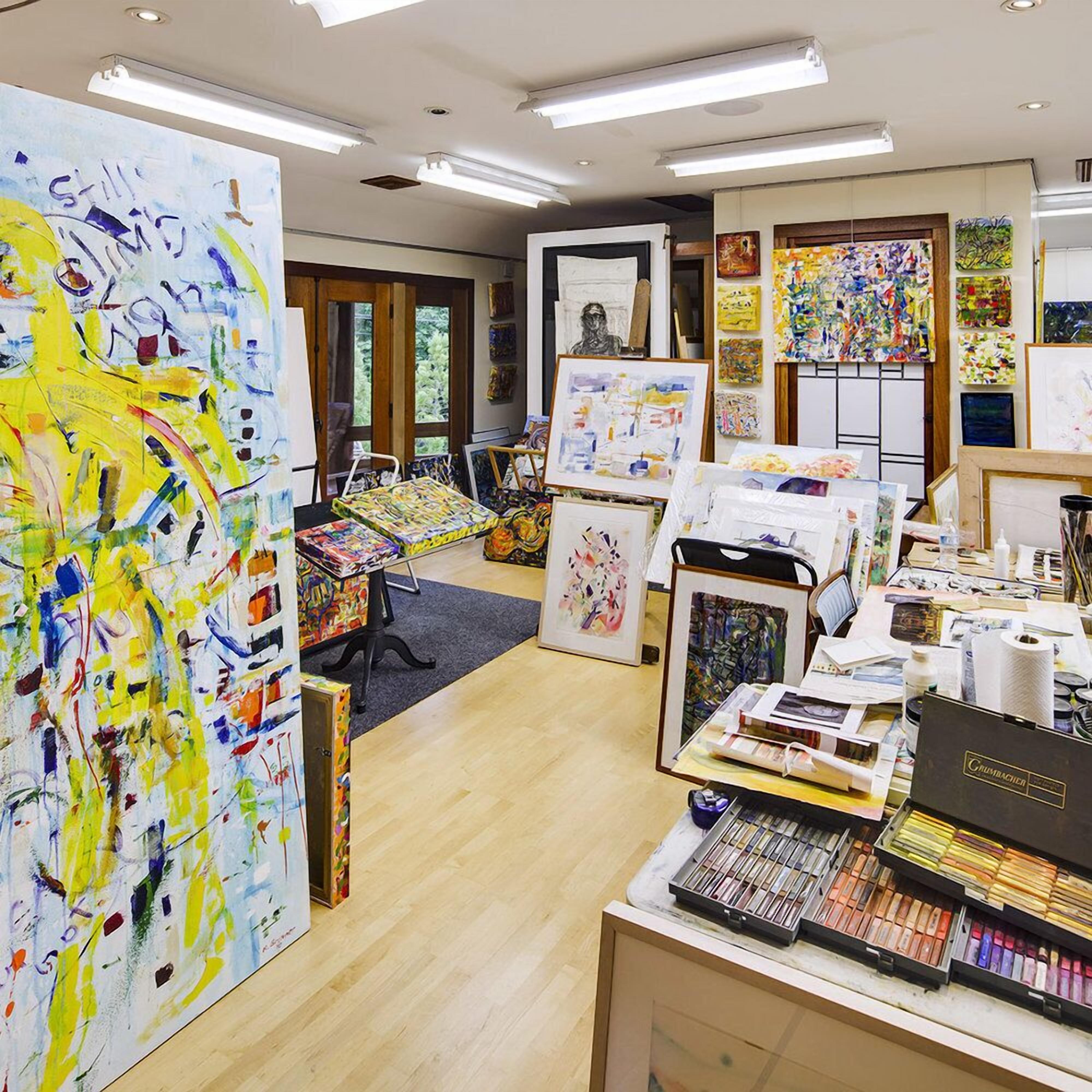 Een kunststudio met verschillende schilderijen en kunstbenodigdheden.