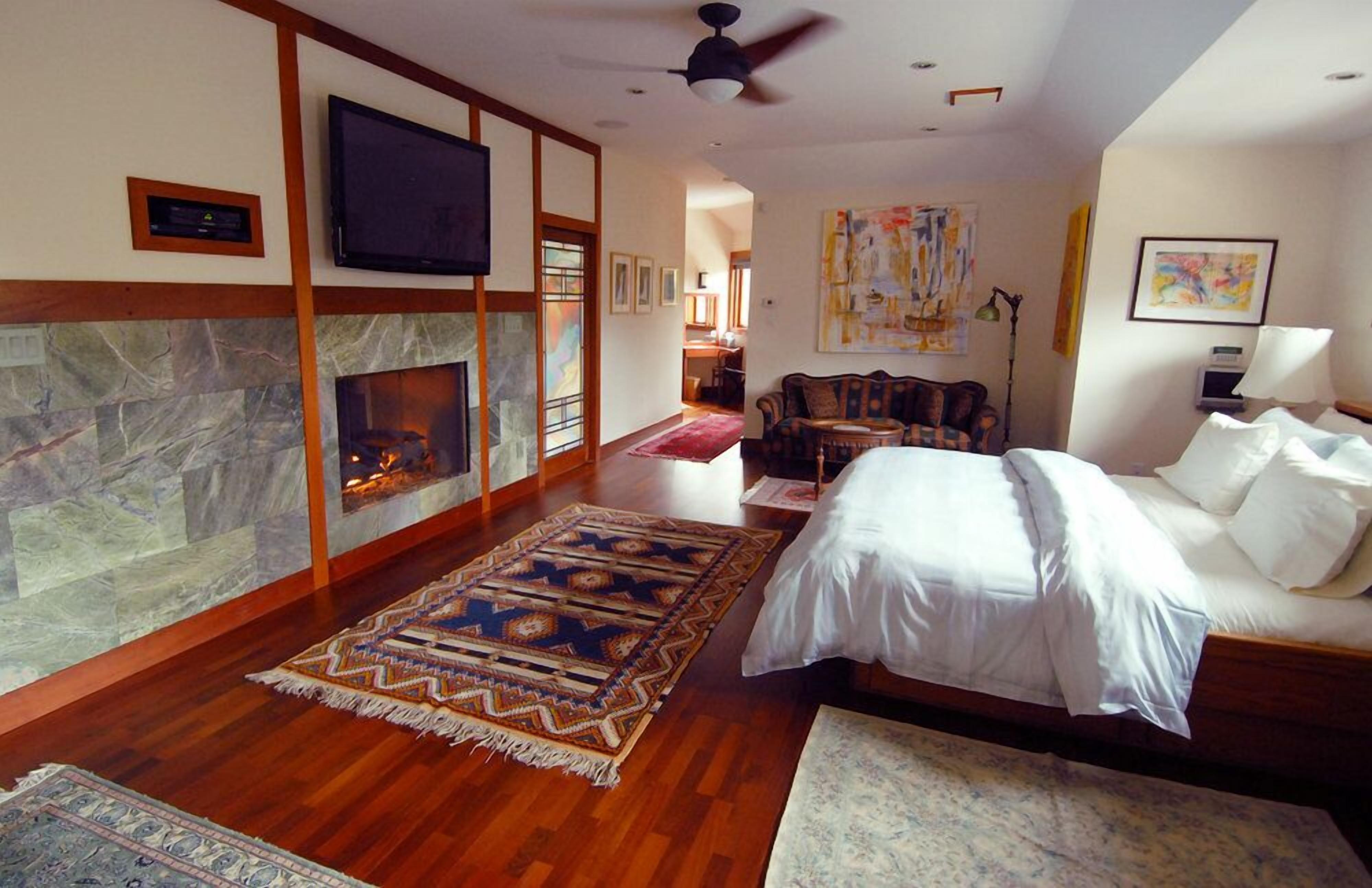 A spacious room with a fireplace, a bed, a TV, and a ceiling fan.