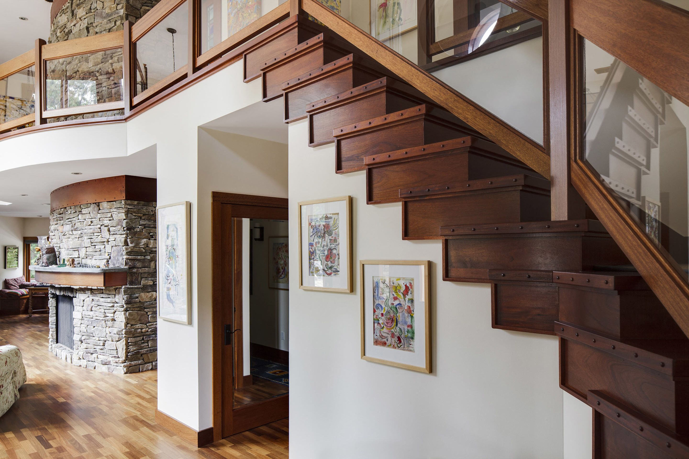 Un vaste espace de vie agrémenté d’un escalier en bois, d’une cheminée en pierre et d’œuvres d’art encadrées qui ornent les murs.
