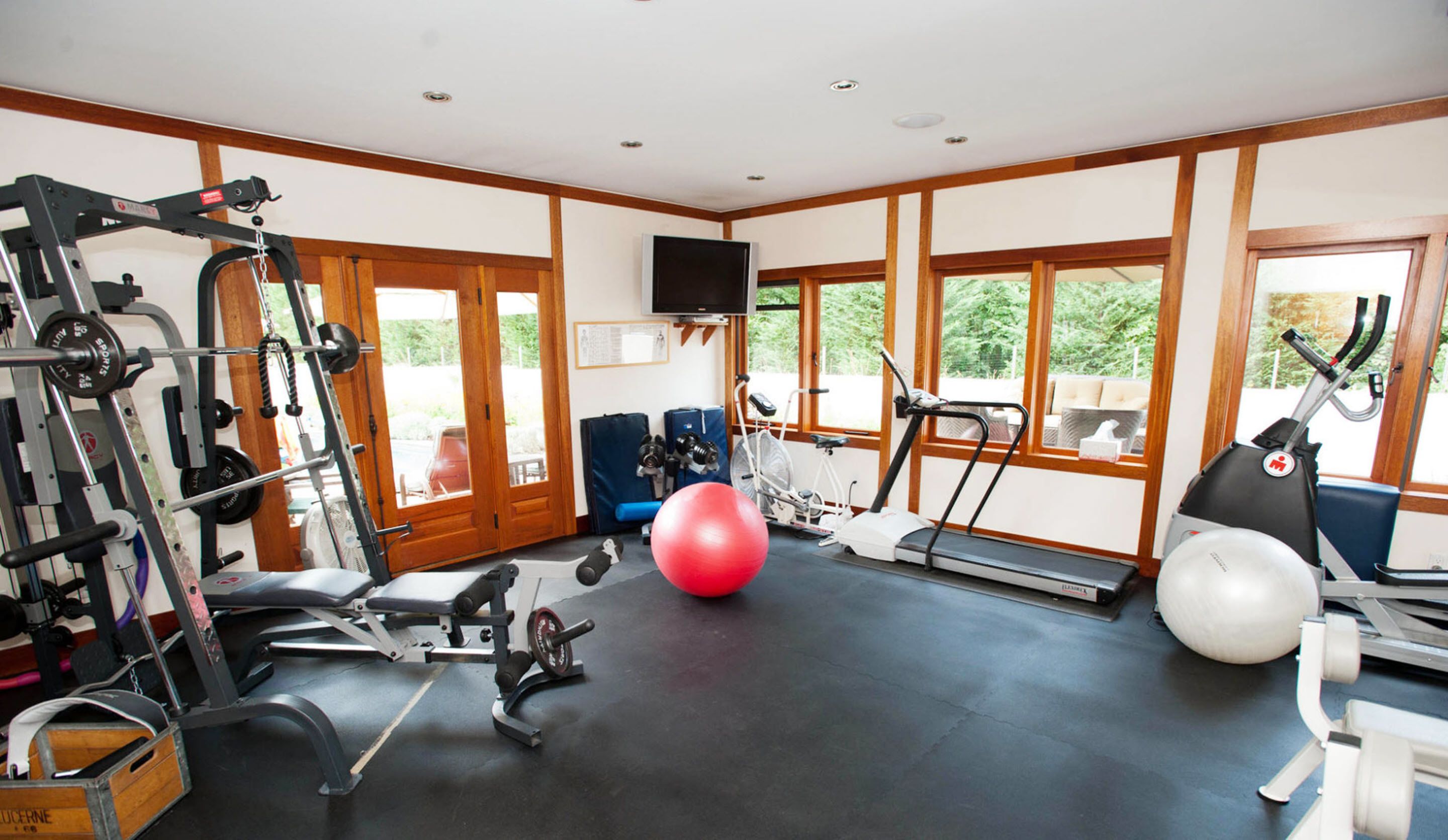 A gym with exercise equipment, a red exercise ball, and large windows offering a view of greenery.