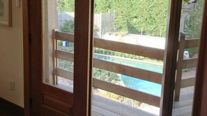 Eine Glastür führt zu einer Außenterrasse mit Blick auf einen Swimmingpool und Grünflächen.