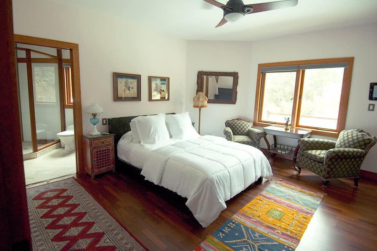 A bedroom with a bed, a chair, a desk, a window, and a door.