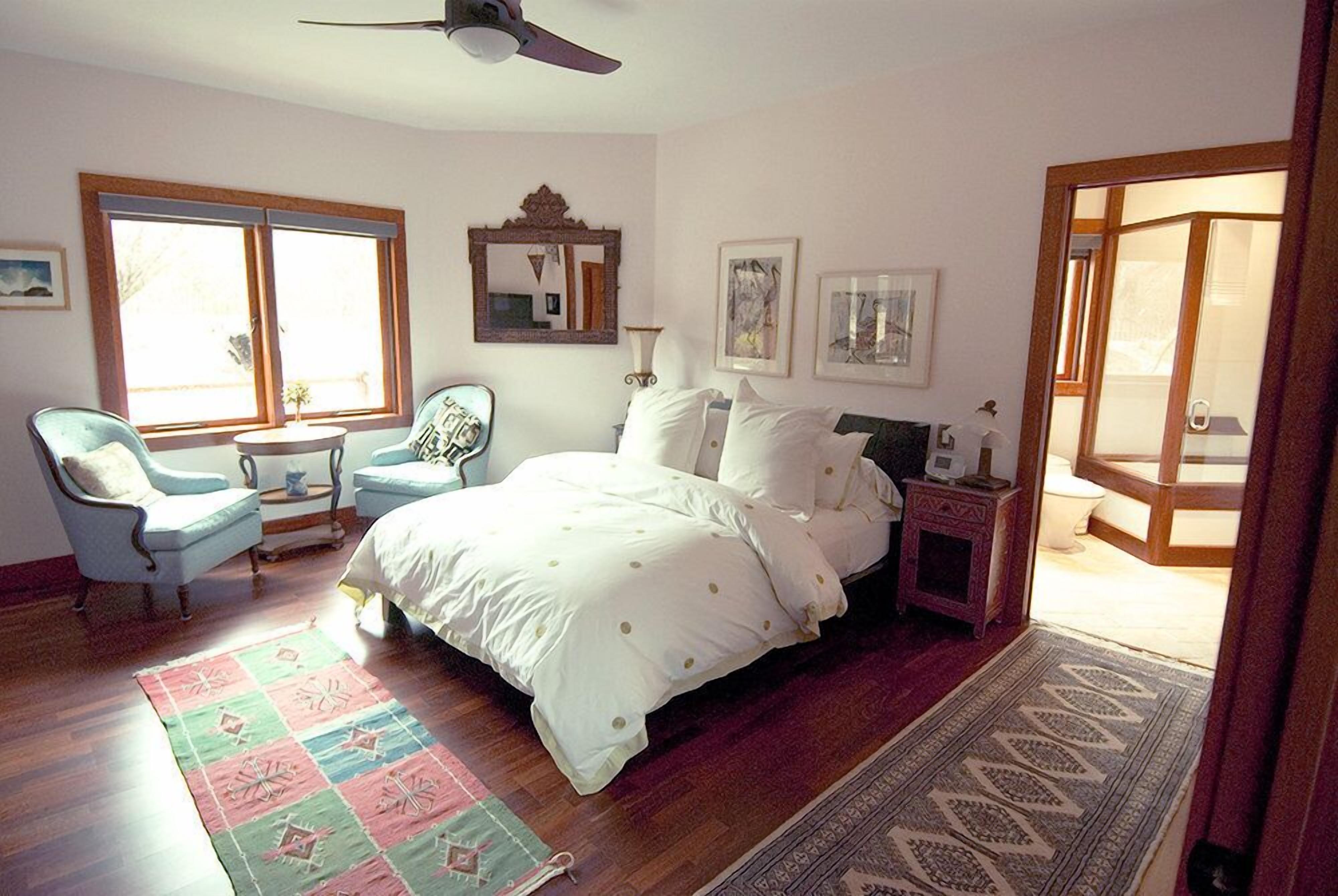 Une chambre à coucher avec un lit, une chaise, une table de chevet, un miroir et une fenêtre.