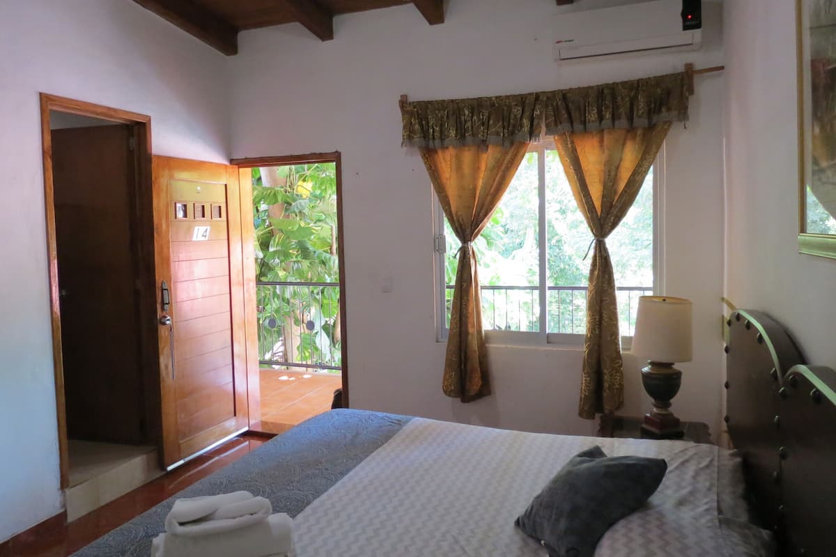 Um quarto com uma cama, janela com cortinas, uma porta e um ar condicionado.