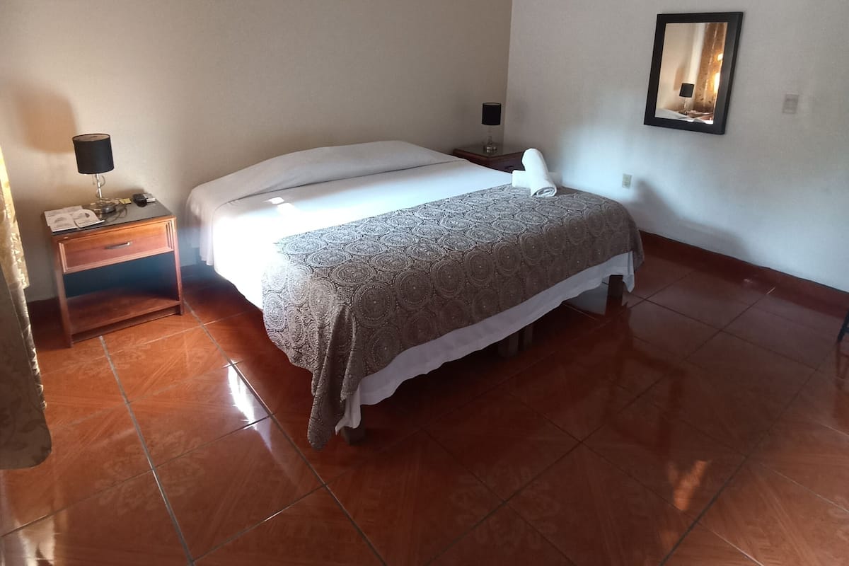 Quarto com cama, mesa de cabeceira, aparelho de ar condicionado e espelho na parede.