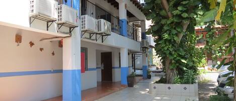 Un edificio de varios pisos con balcones, unidades de aire acondicionado y un patio con azulejos.