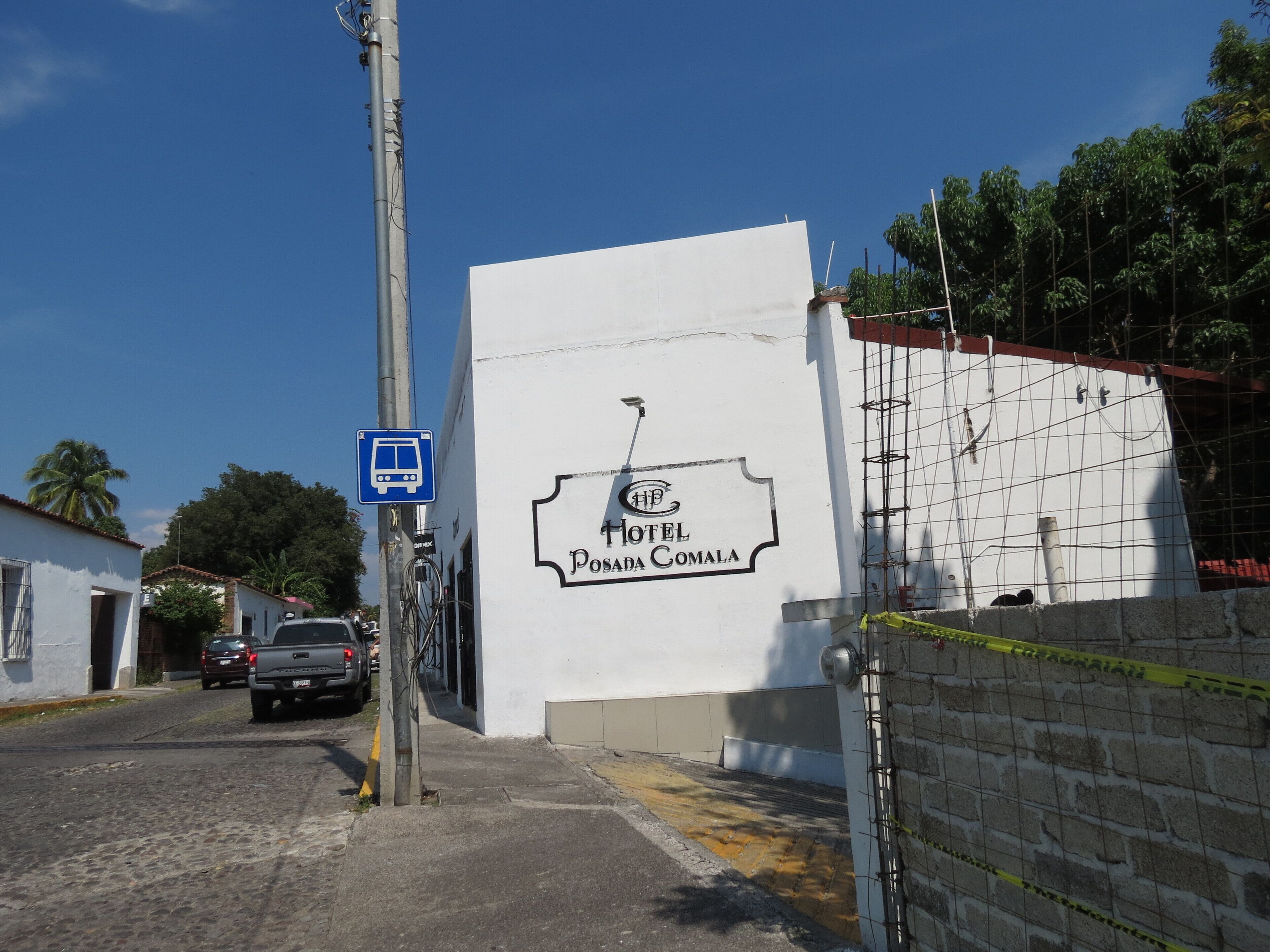 Un edificio blanco con un cartel que dice 'Hotel Posada Comala' y una señal de parada de autobús azul.