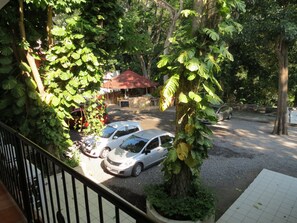 A parking area with two cars, surrounded by lush greenery and a building with a red roof.