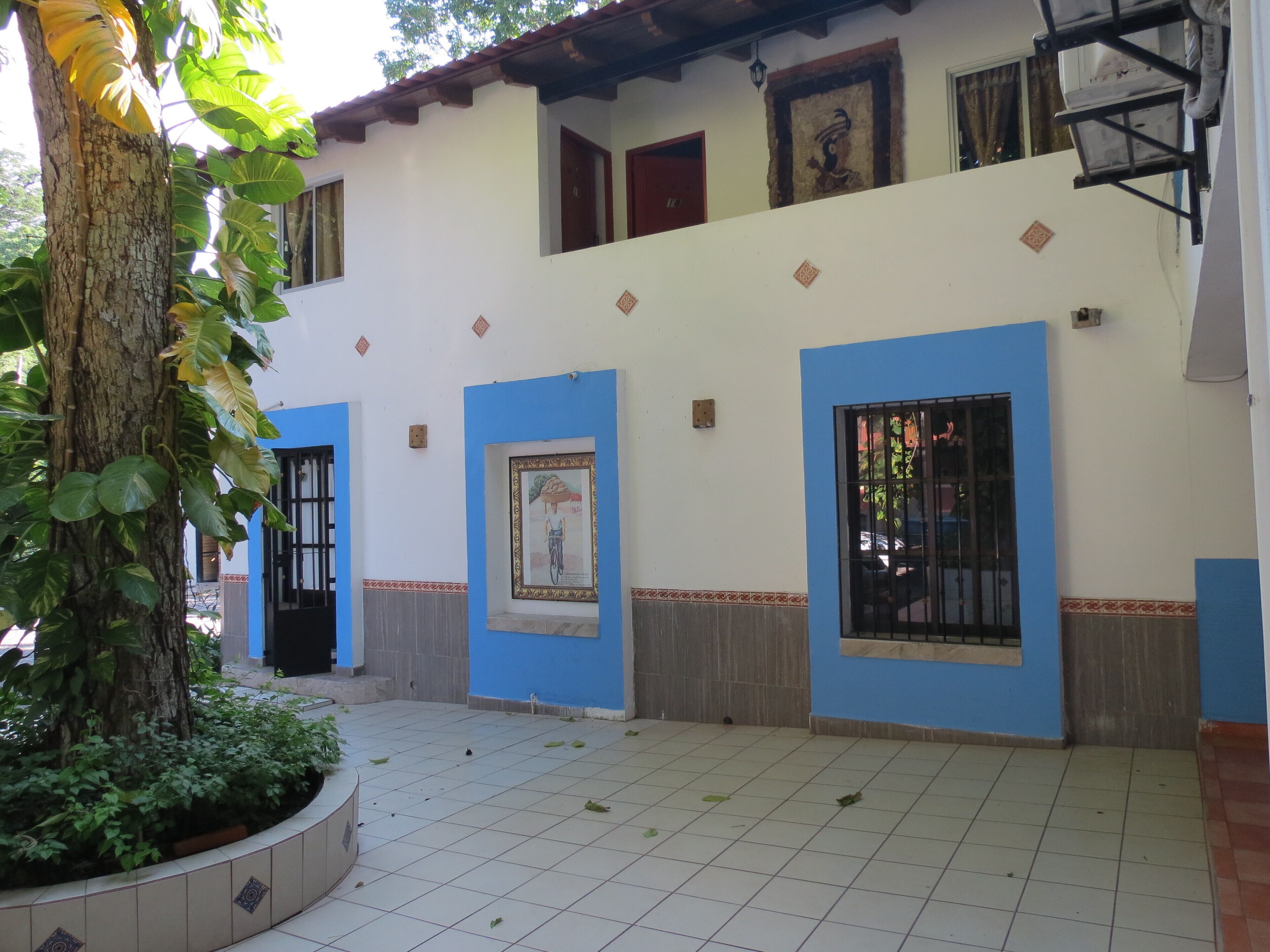 A building with blue doors and windows, a tiled courtyard, and a tree with green leaves.