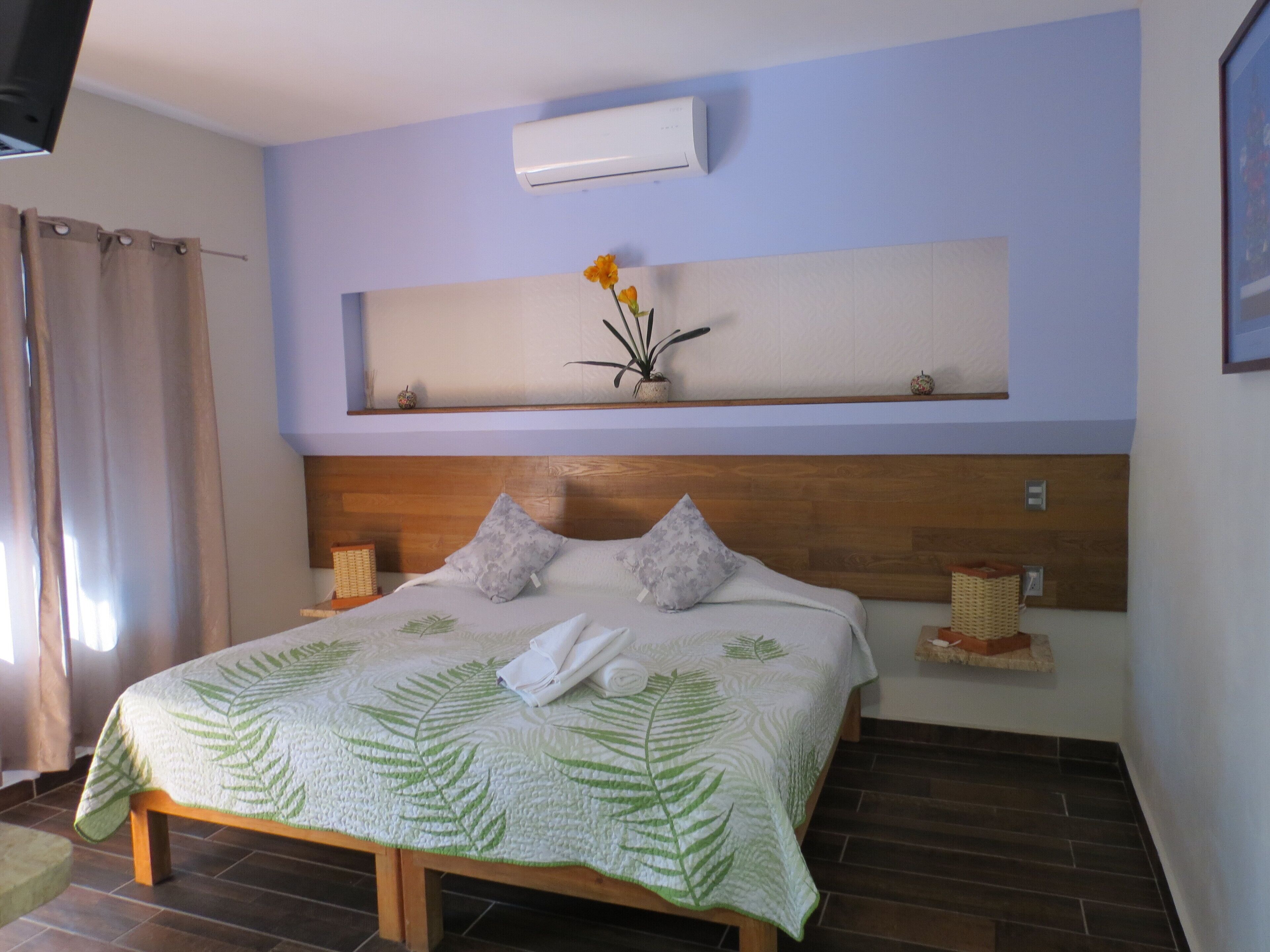 Un dormitorio con cama, aire acondicionado de pared, estante con adornos y ventana con cortinas.