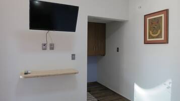 Una habitación con un televisor montado, un estante de madera, un cuadro enmarco y un acceso a otra estancia.