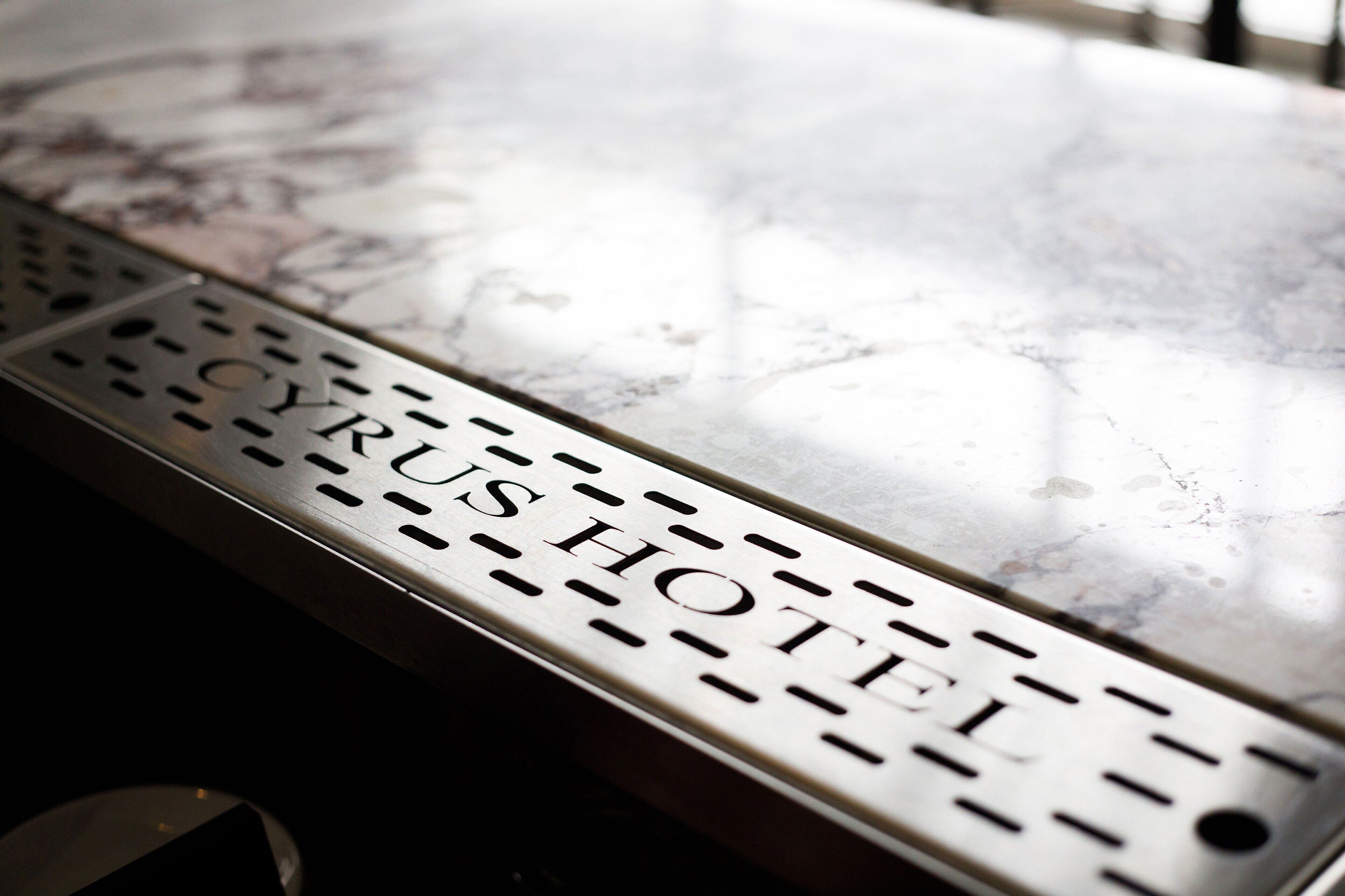 A metal sign with the text "CYRUS HOTEL" on a marble surface.