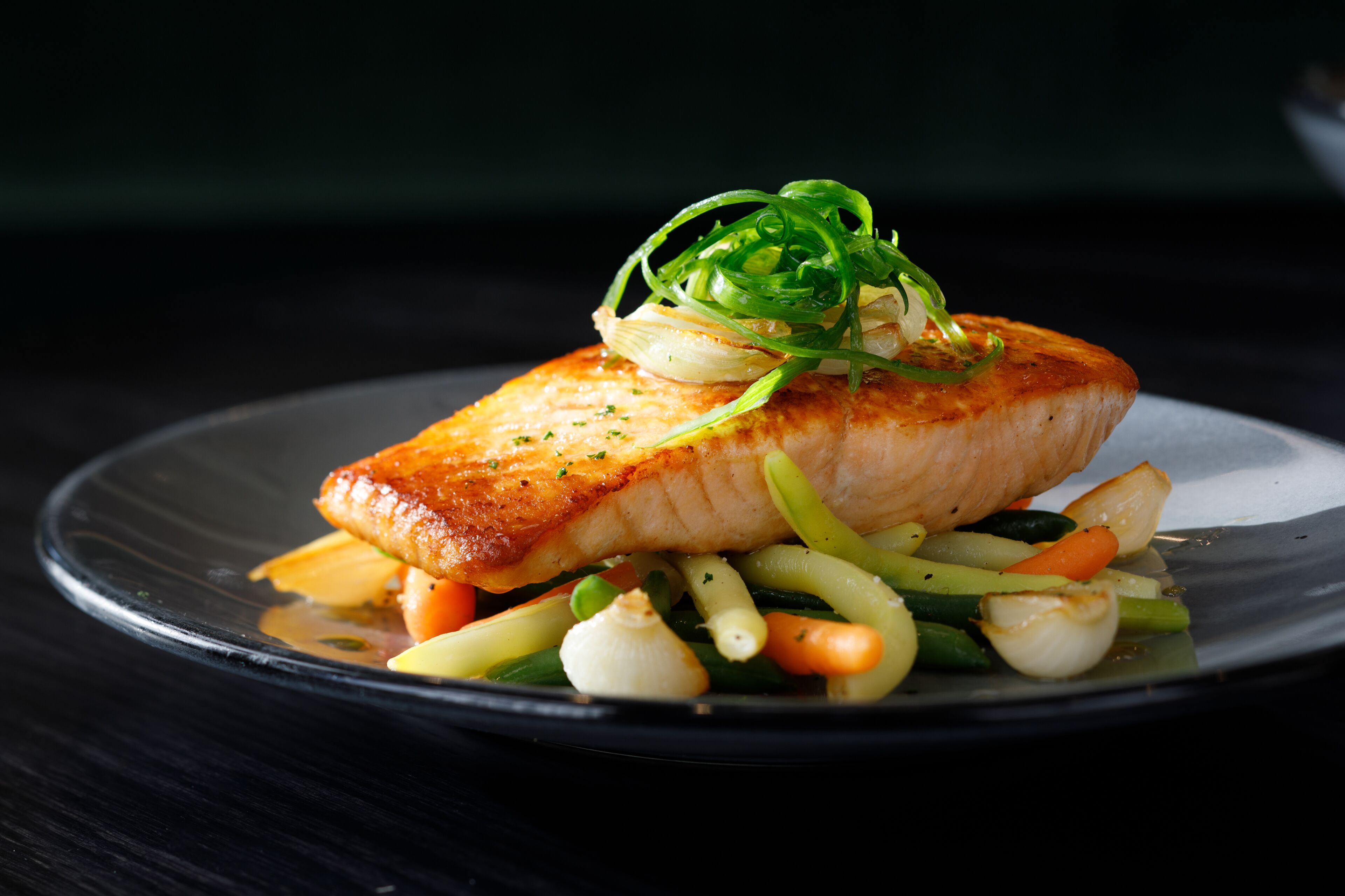 A plate with a piece of salmon, vegetables, and a garnish.