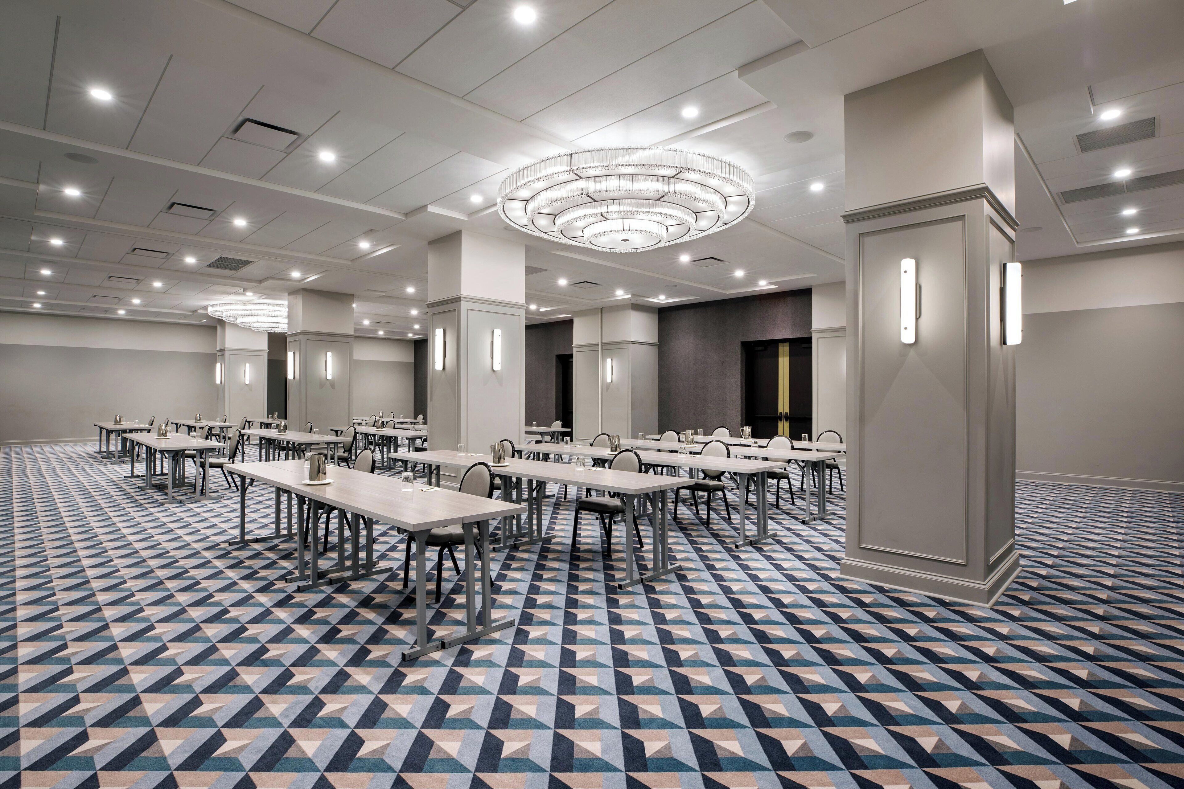 A conference room with multiple tables and chairs, a patterned floor, and a modern chandelier.