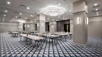 A conference room with multiple tables and chairs, a patterned floor, and a modern chandelier.