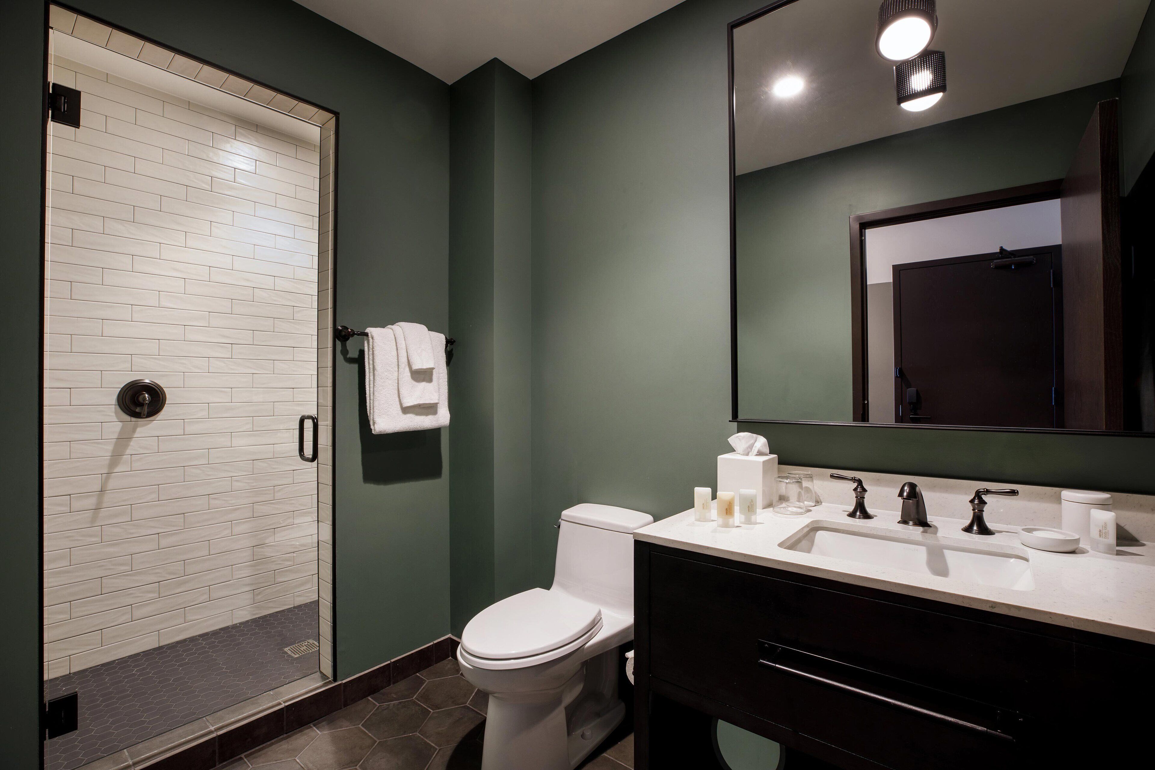 A modern bathroom with a white toilet, a glass shower enclosure, a white sink with a black vanity, and a mirror above the sink.