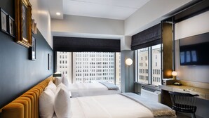 Ein modernes Hotelzimmer mit zwei Betten, einem Schreibtisch und einem großen Fenster mit Blick auf die Stadt.