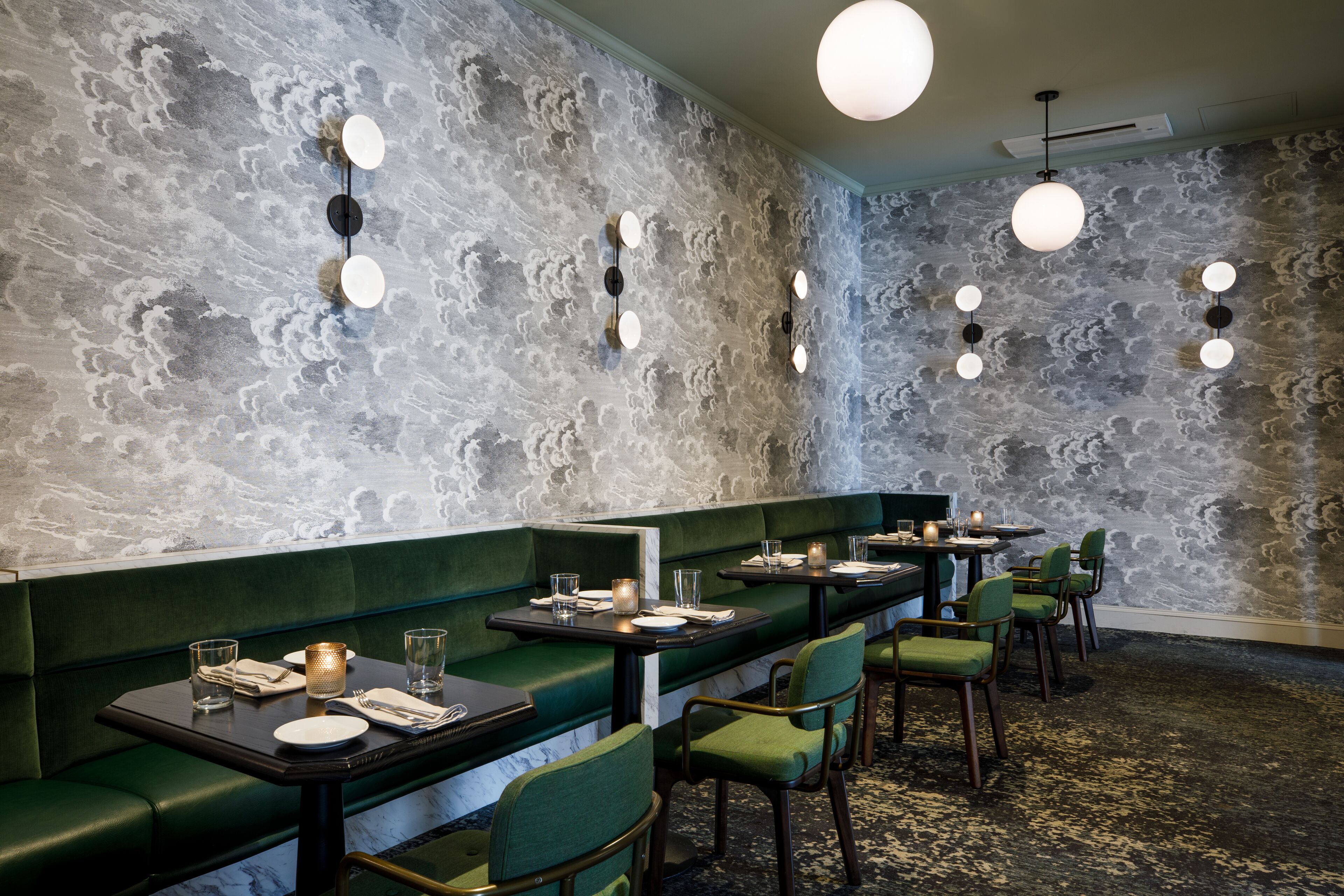 A restaurant with green booths, round tables, and a textured wall.