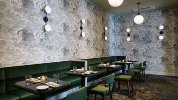 A restaurant with green booths, round tables, and a textured wall.