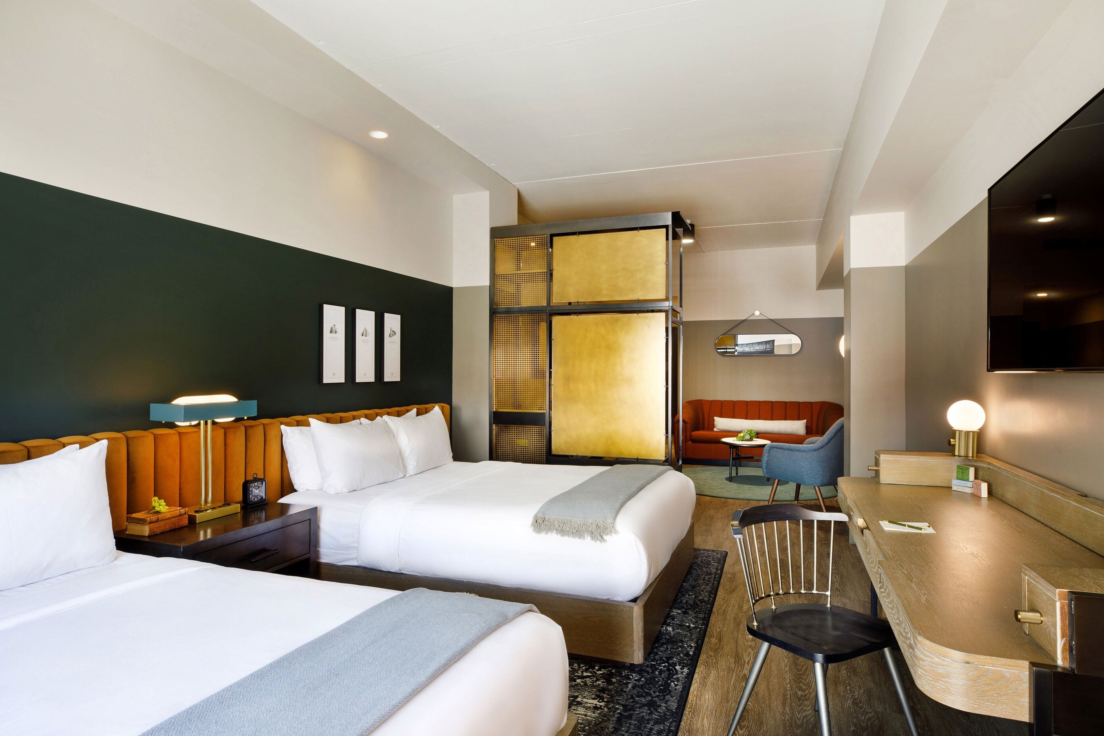 Habitación de hotel con dos camas, un escritorio, una silla, un sofá y un televisor.