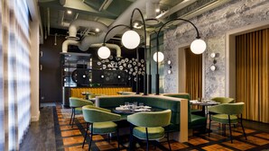 Ein modernes Restaurant mit grün bezogenen Sitzmöglichkeiten, einer zentralen Bar und einem gemusterten Boden.