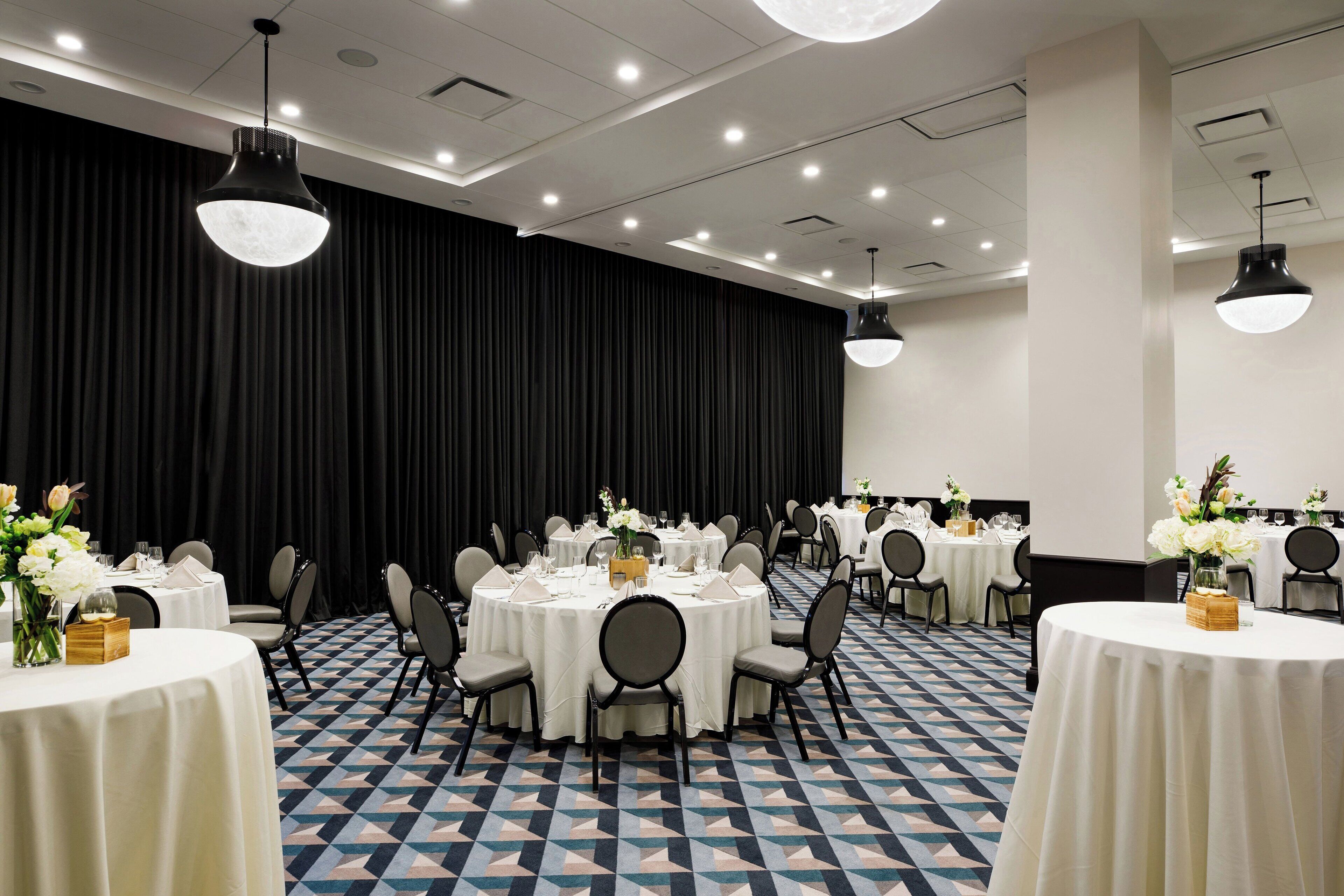 A conference room with round tables, chairs, and a black curtain backdrop.