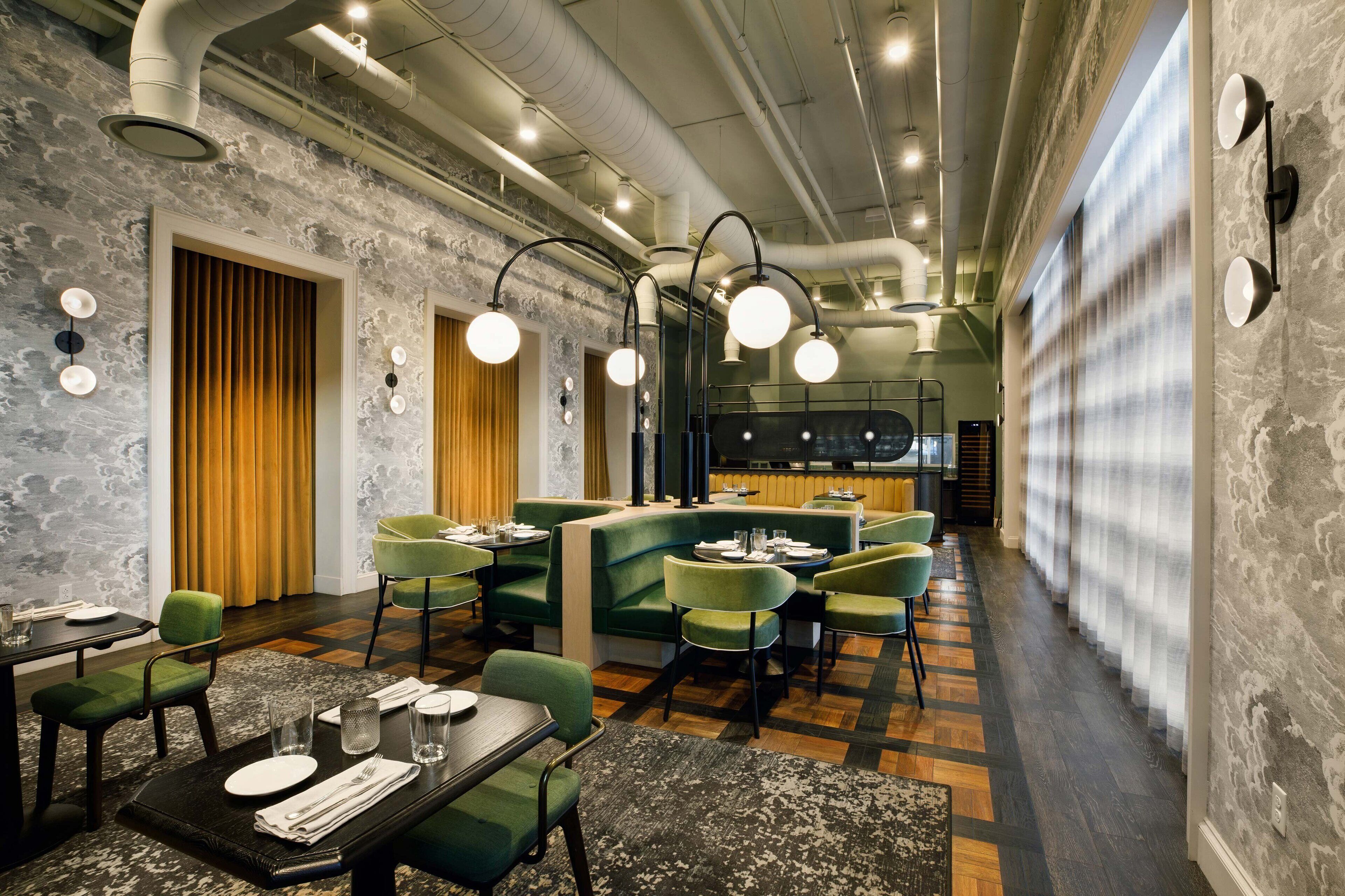 Un restaurant moderne avec des banquettes et des tables vertes, des conduits apparents et un mélange de murs en bois et en pierre.