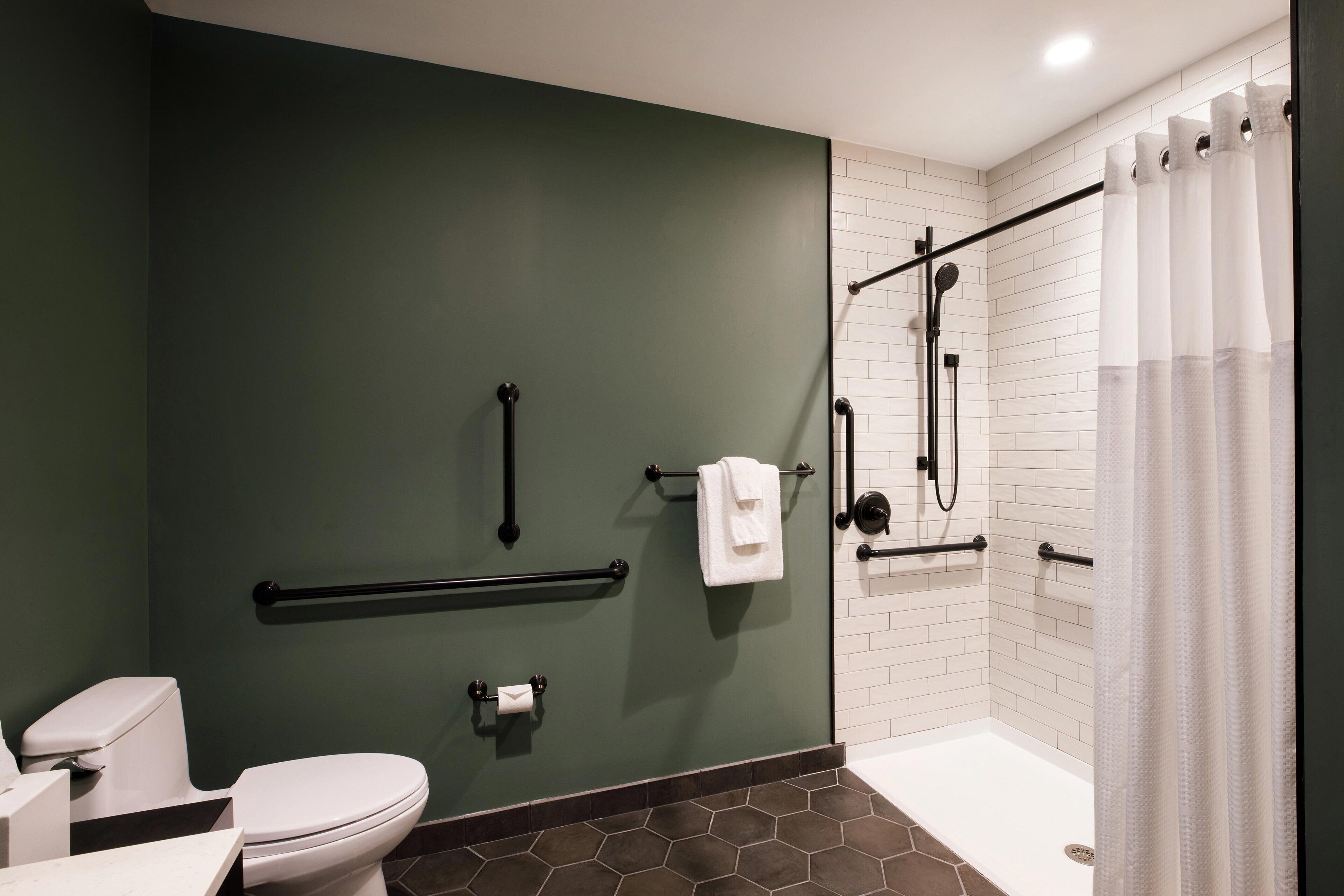 A modern bathroom with a green wall, white tiles, a white toilet, a shower with a glass door, and a towel rack.