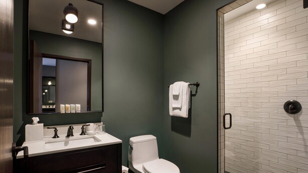 A modern bathroom with a dark green wall, white tiled shower, and a white toilet. - Cyrus Hotel, Topeka, a Tribute Portfolio Hotel (Topeka)