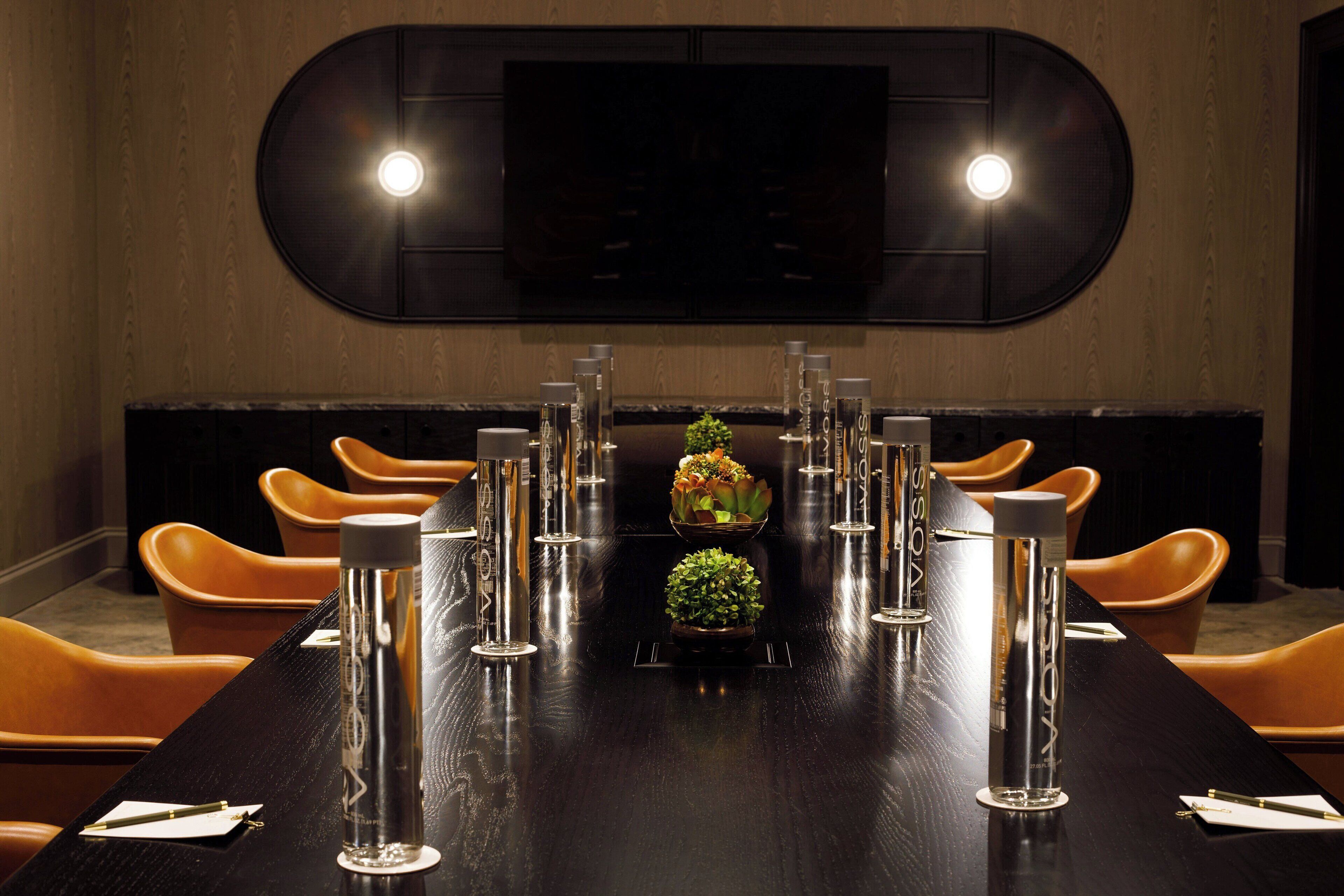 Un salón de conferencias con una larga mesa, sillas y una pantalla de televisión en la pared.