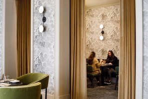 A dining area with green chairs, a table set for two, and a wall with a textured pattern.