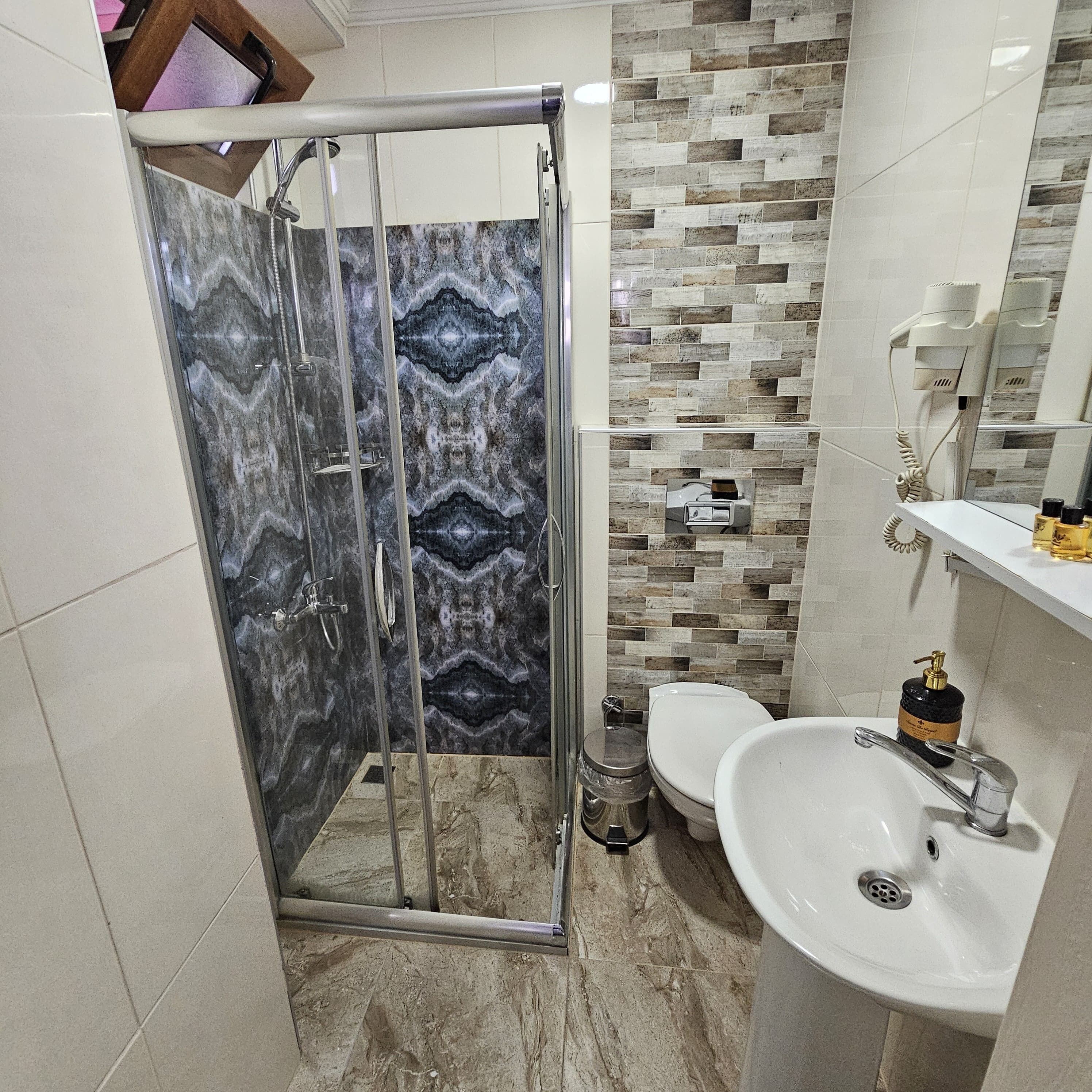 A bathroom with a shower, toilet, sink, and a mirror.