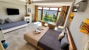 Une chambre avec un lit, un canapé, une télévision, une fenêtre donnant sur la ville et une petite table avec une chaise.
