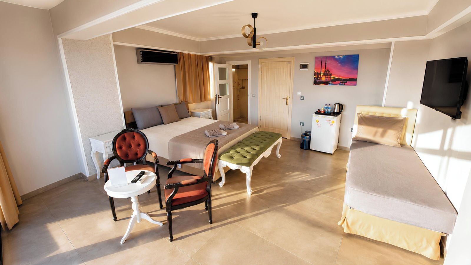 A hotel room with a bed, a desk, a chair, a bench, a television, and a painting on the wall.