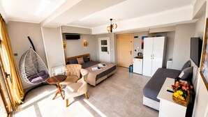 Una habitación de hotel moderna con cama, sofá, mesa de comedor, sillón colgante, kitchenette y televisor.