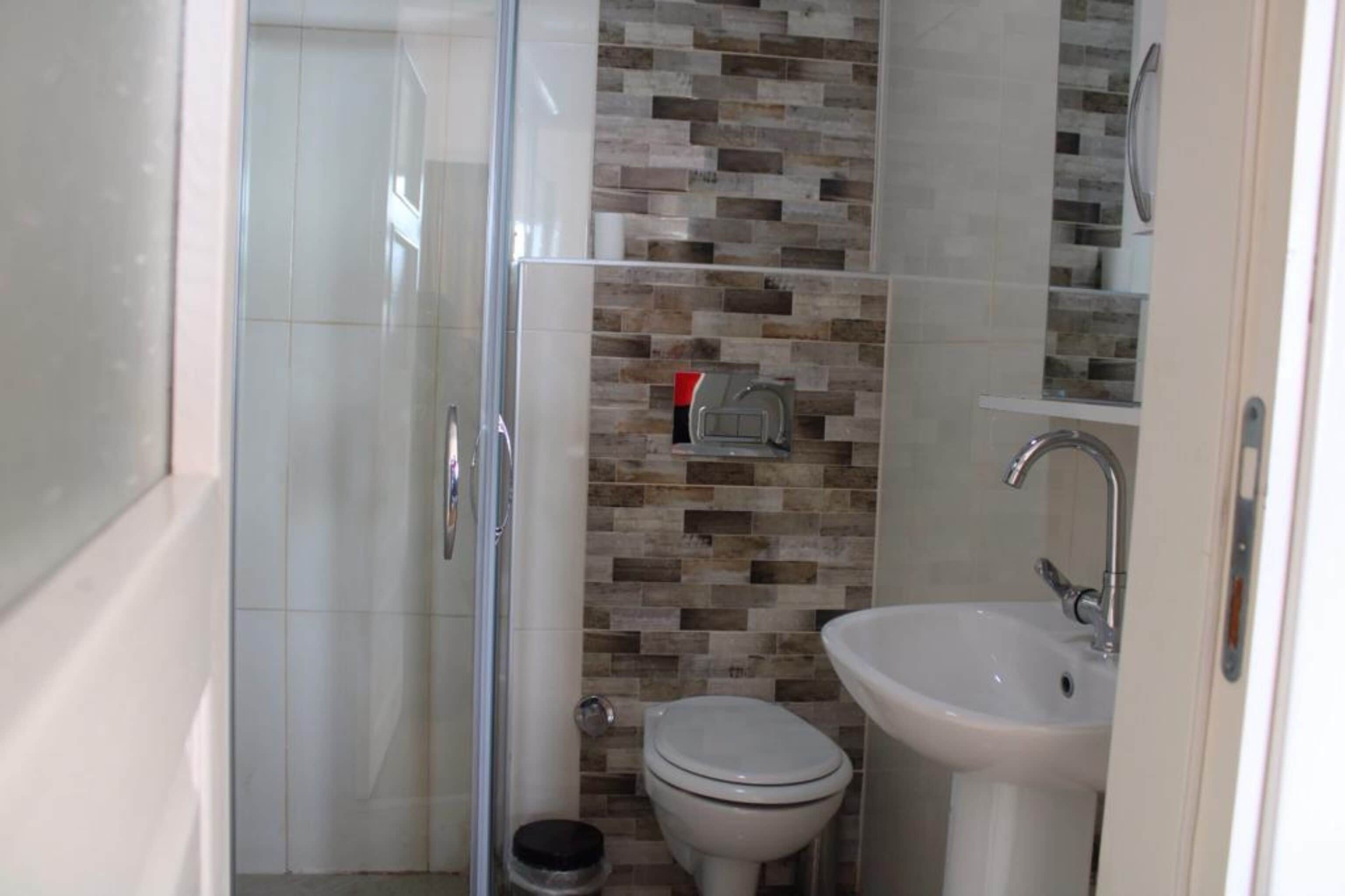 A bathroom with a glass shower enclosure, a toilet, and a sink with a mirror above it.