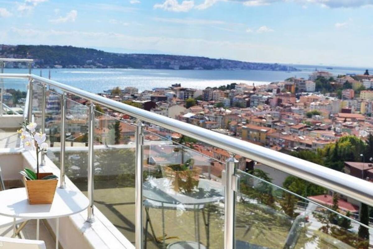 Varanda com guarda-corpo de vidro, vista para a cidade e para a água.