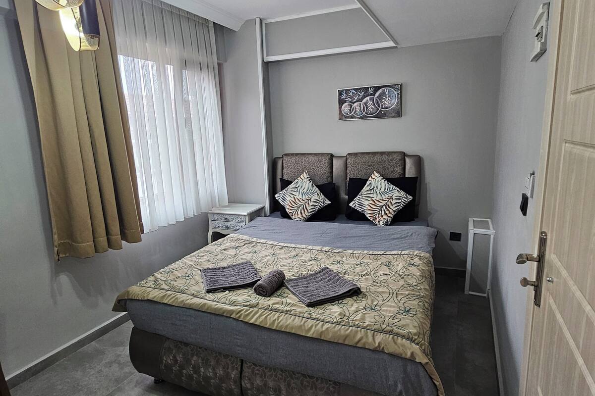Um quarto com cama, mesa de cabeceira, luminária de teto e um quadro na parede.
