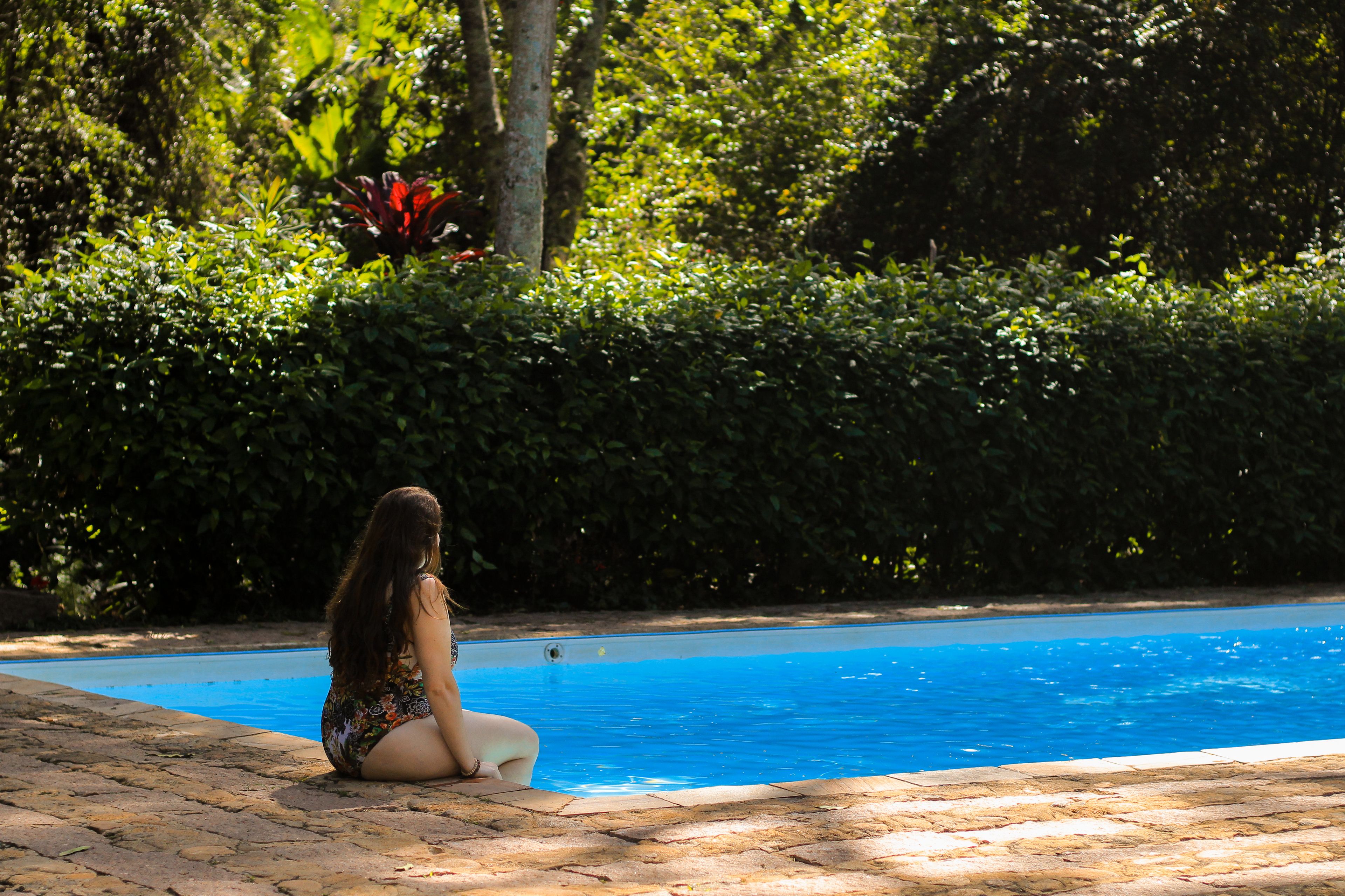 Una dona asseguda al costat d'una piscina, amb vegetació exuberant al fons.