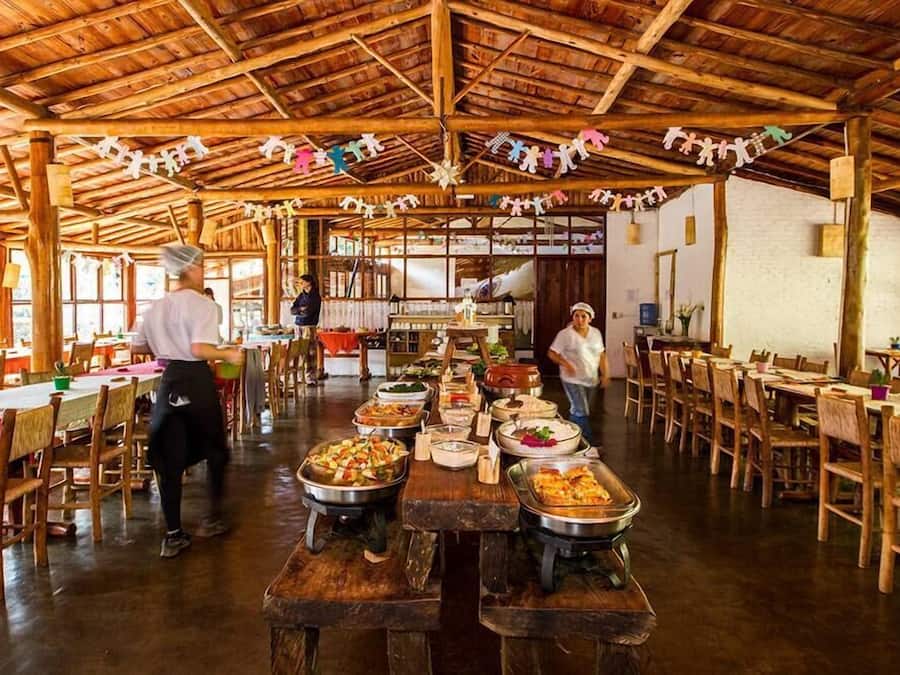 Une vaste salle à manger dotée de tables et de bancs en bois, d’un haut plafond également en bois, et où une variété de plats sont présentés sur les tables.