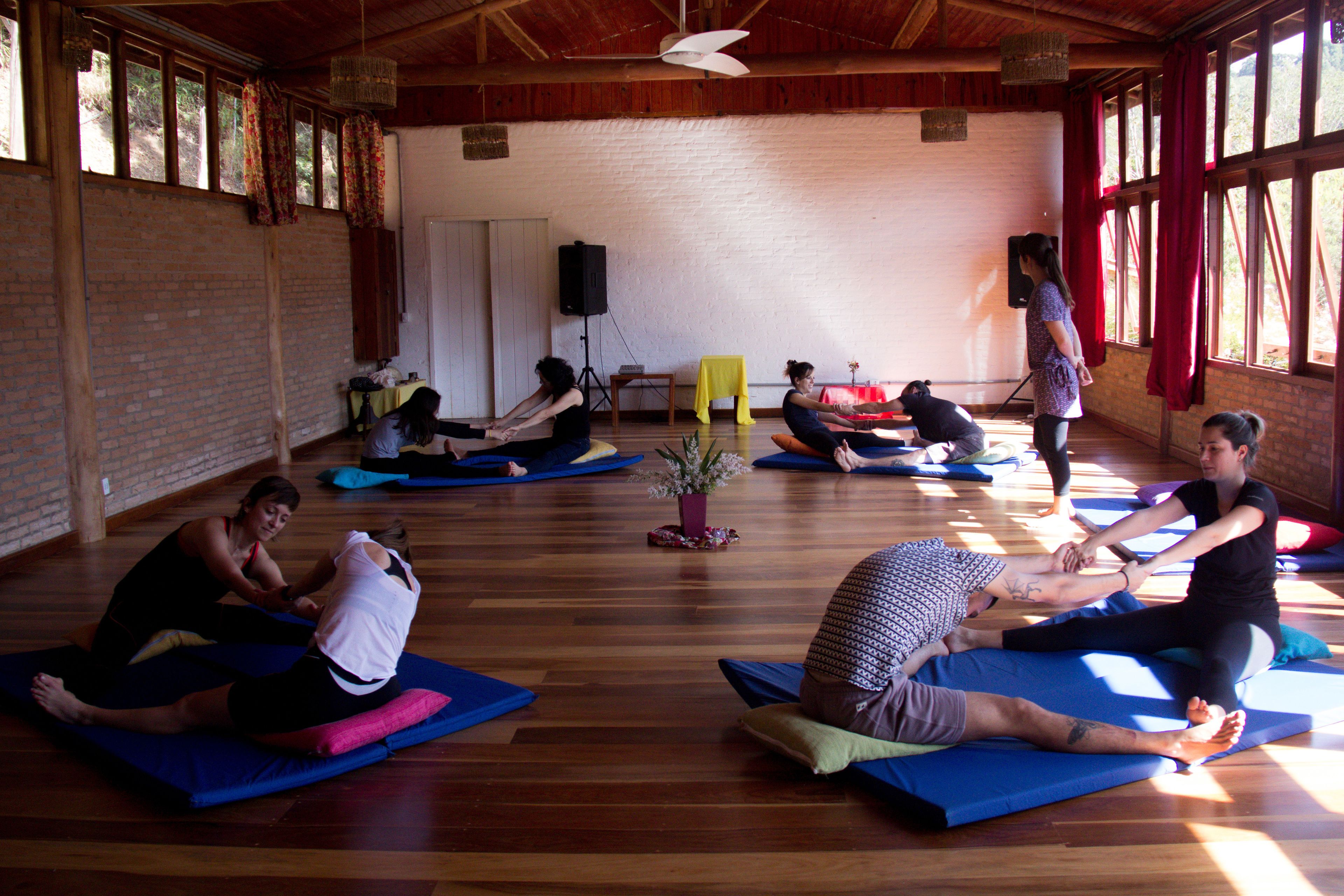 Una clase de yoga en una habitación con paredes de ladrillo, pisos de madera y ventanas amplias.